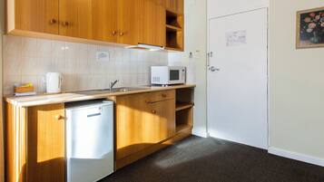 A compact kitchen with wooden cabinets, a microwave, a small refrigerator, and a sink.