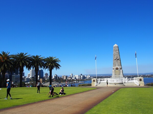A park with a monument, palm trees, and a city skyline in the background.