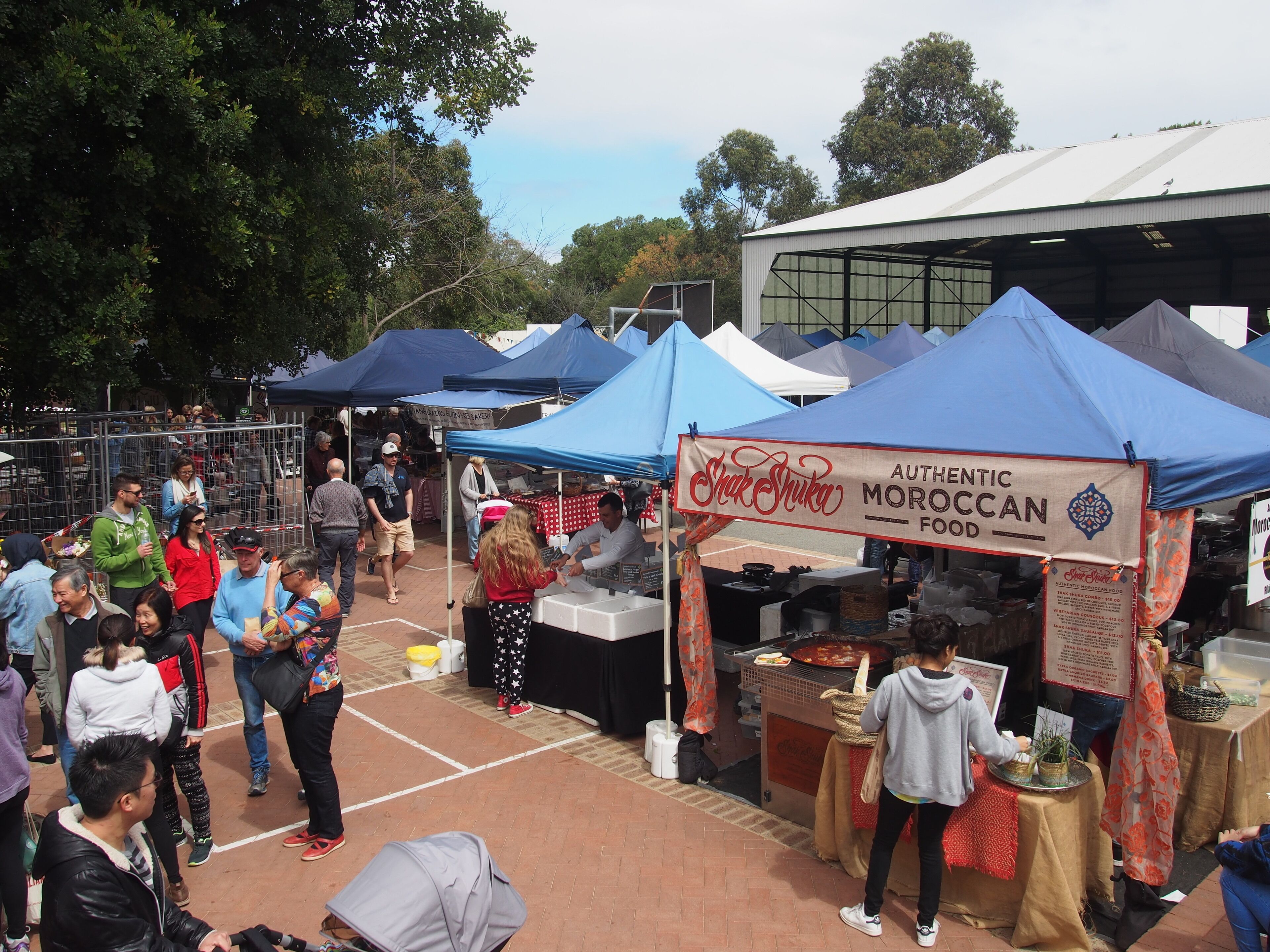 A bustling outdoor market with various food stalls, including one labeled "Authentic Moroccan Food."