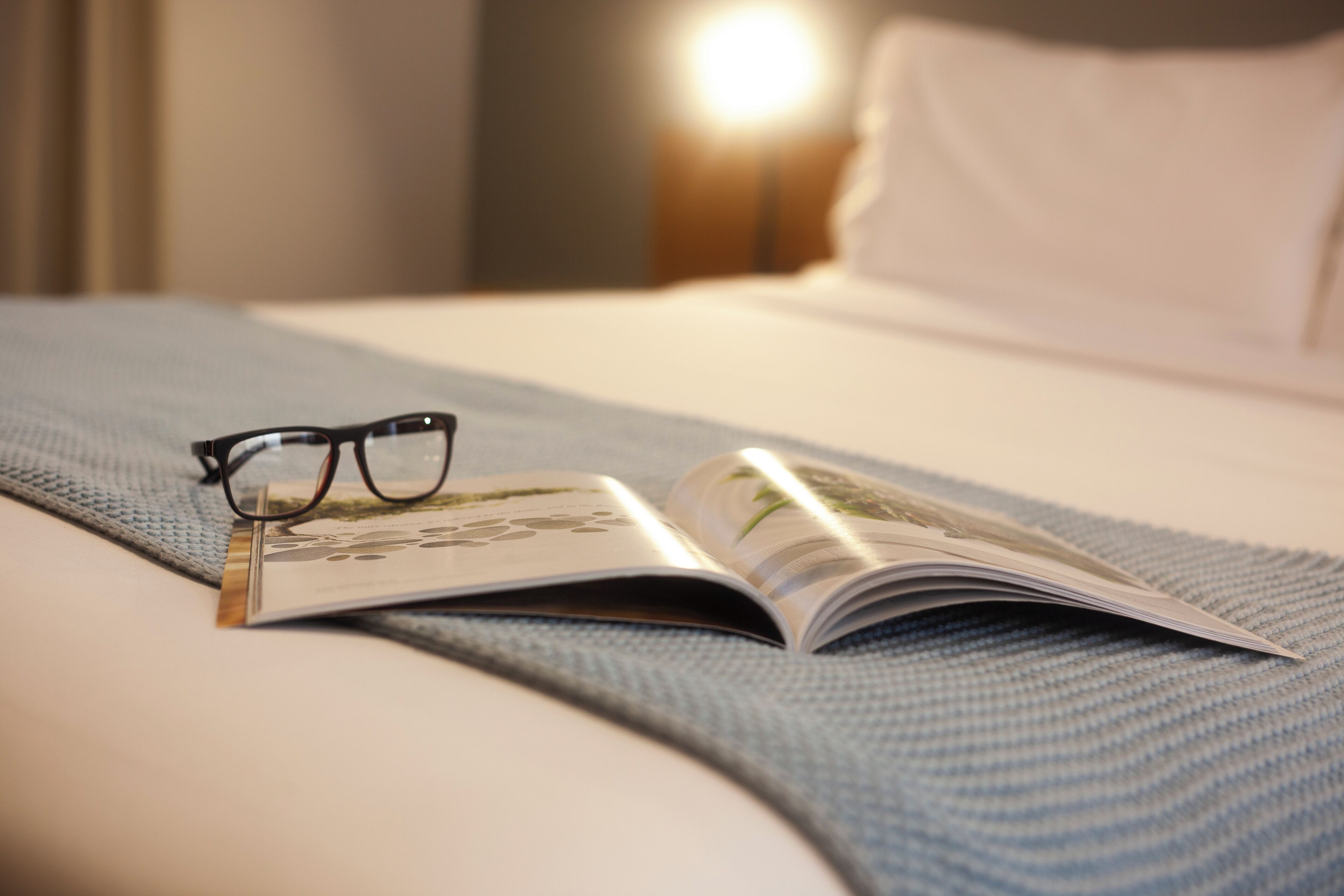 A neatly made bed with a magazine and glasses on it.