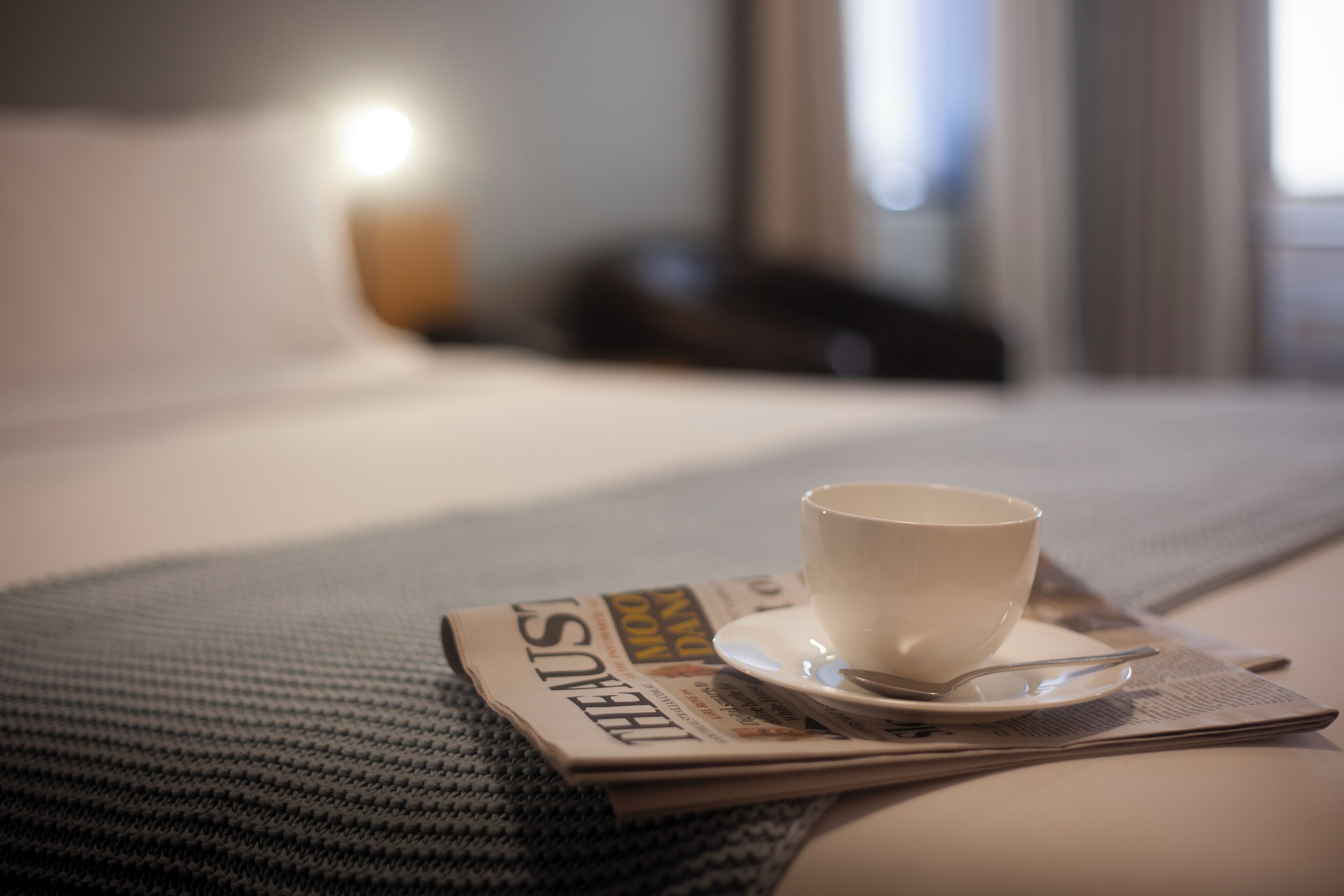 Un letto con un giornale, una tazza e un cucchiaio su un tavolo.