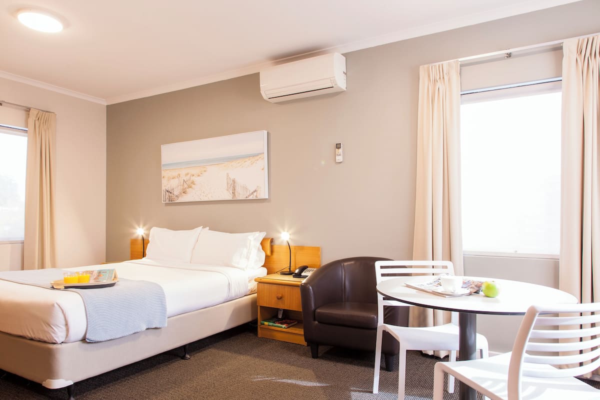 Ein Hotelzimmer mit Bett, Nachttisch, Lampe, Sessel und einem kleinen Esstisch mit Stühlen.