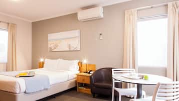 A hotel room with a bed, bedside table, lamp, chair, and a small dining table with chairs.