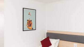 A modern hotel room with a single bed, a headboard, a small bedside table, and a wall-mounted artwork.