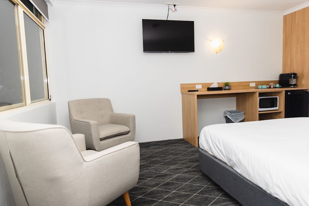 A hotel room with a bed, a chair, a desk with a TV, a microwave, and a coffee machine.