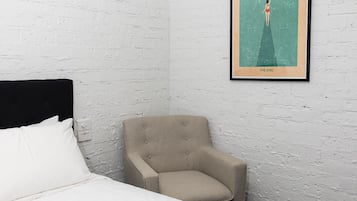 A bedroom with a bed, a chair, and a framed poster on the wall.