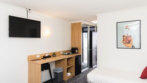 A hotel room with a bed, a desk with a coffee machine, a TV, and a trash bin.