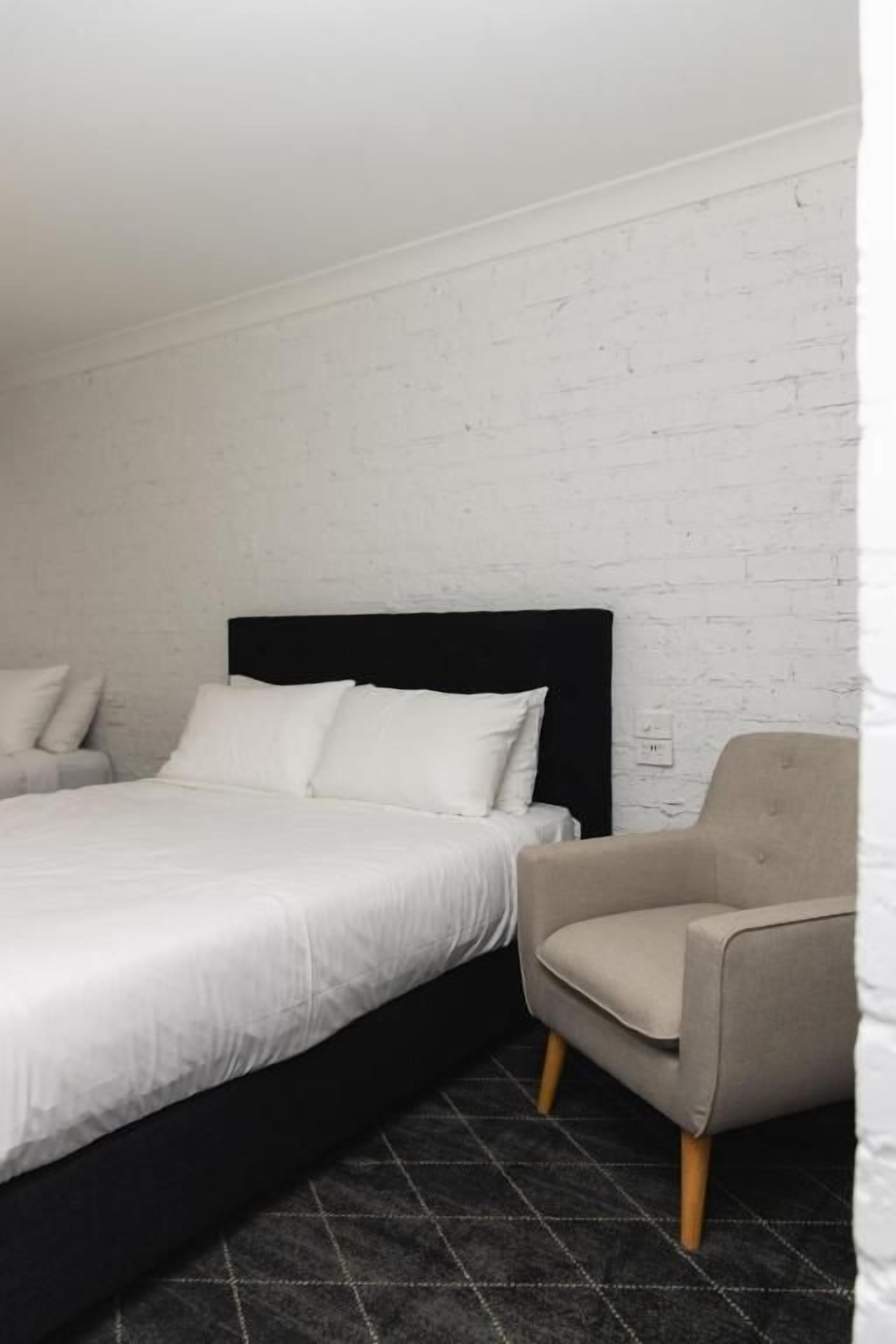 A bedroom with a bed, a chair, and a white brick wall.