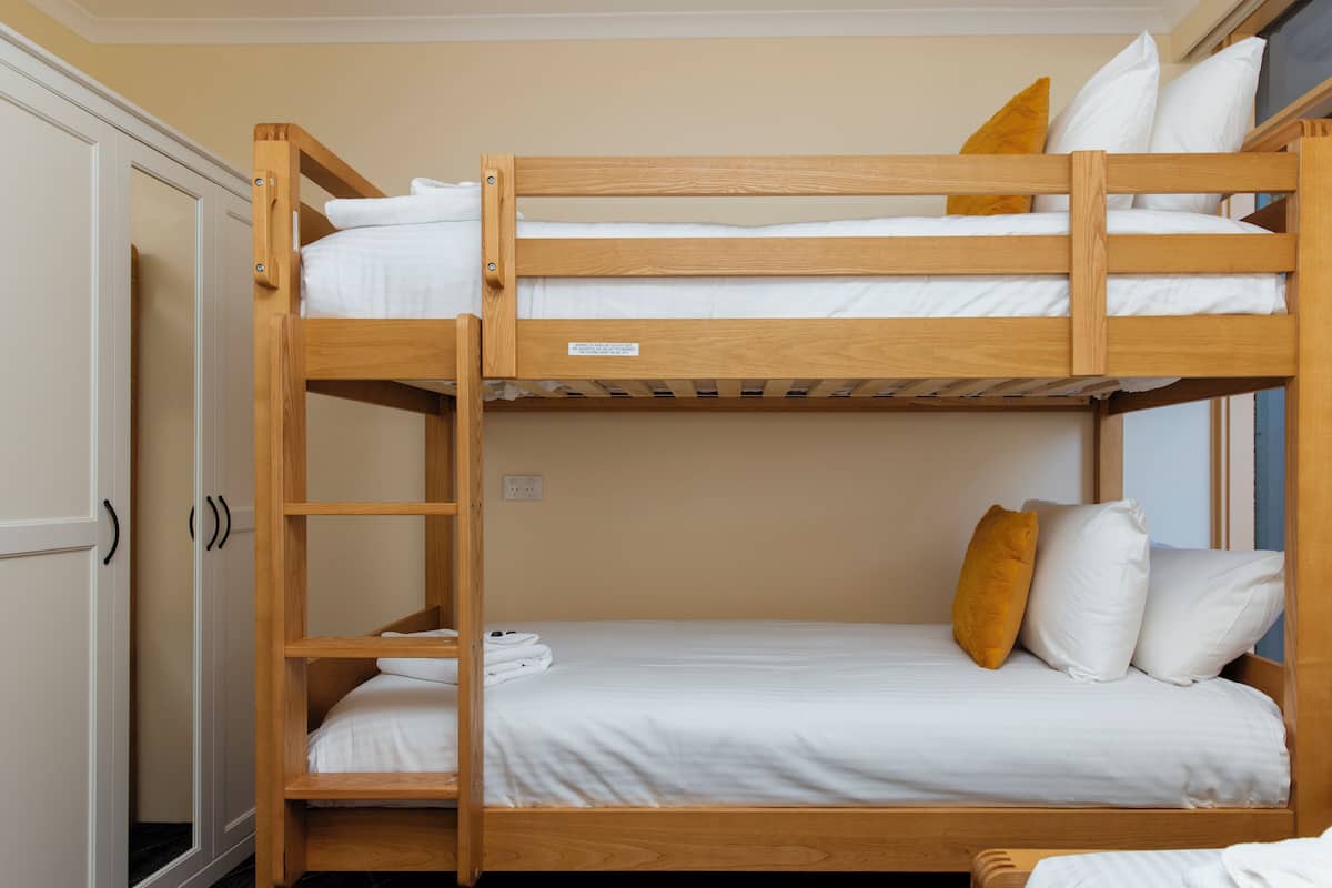 A bunk bed with white bedding and a wooden frame.