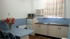 A compact kitchen with a microwave, a small refrigerator, and a sink. There is a dining table with chairs and a vase with flowers. - Golden Fountain Motel (Allenstown)