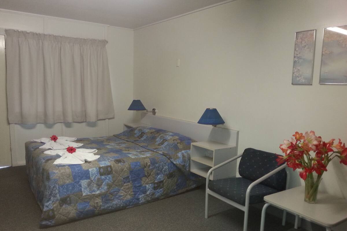 Hotellihuone, jossa on sänky, tuoli, pieni pöytä ja ikkuna, jossa on verhot.