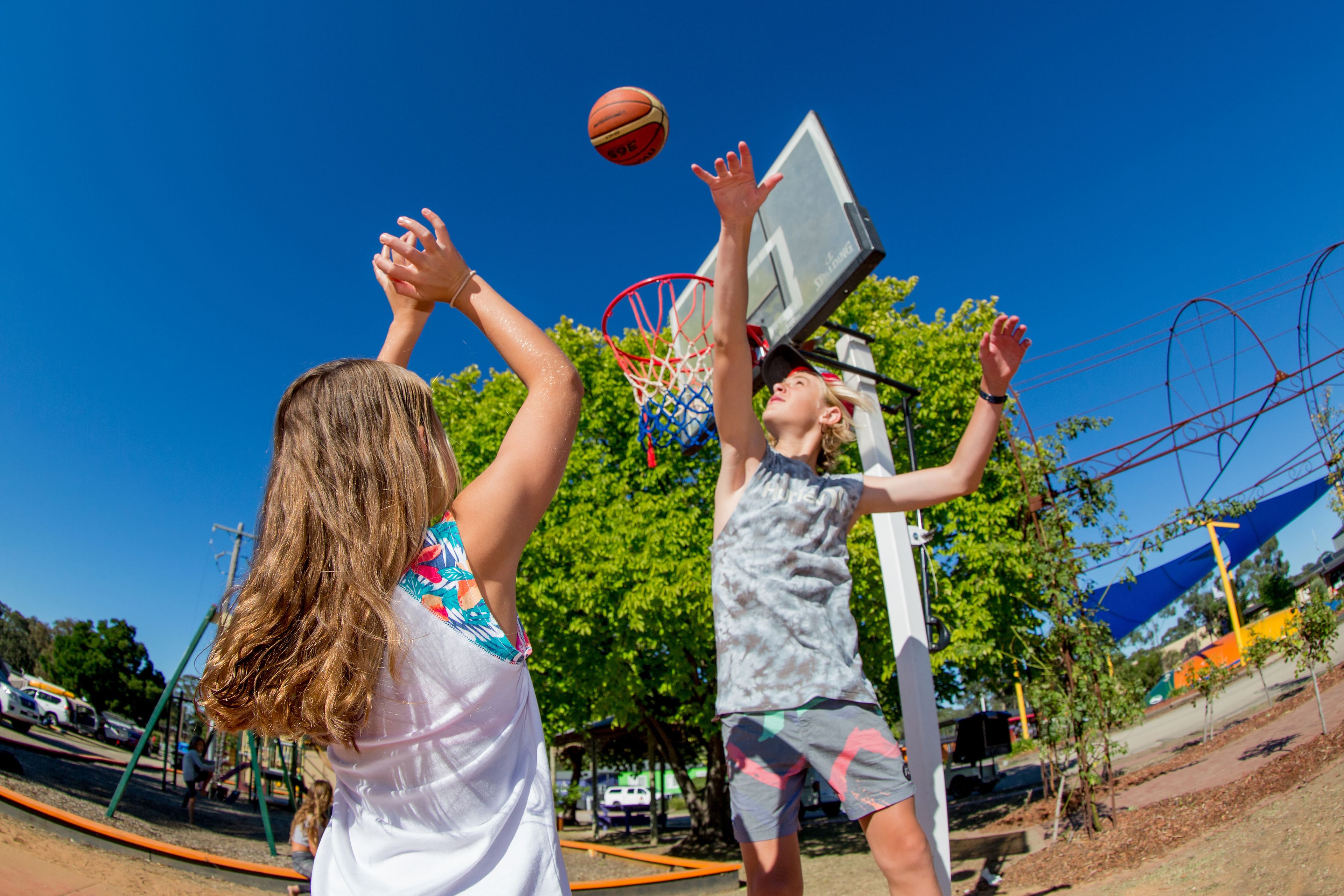 Due persone giocano a basket in un campo da gioco all'aperto sotto un cielo azzurro.