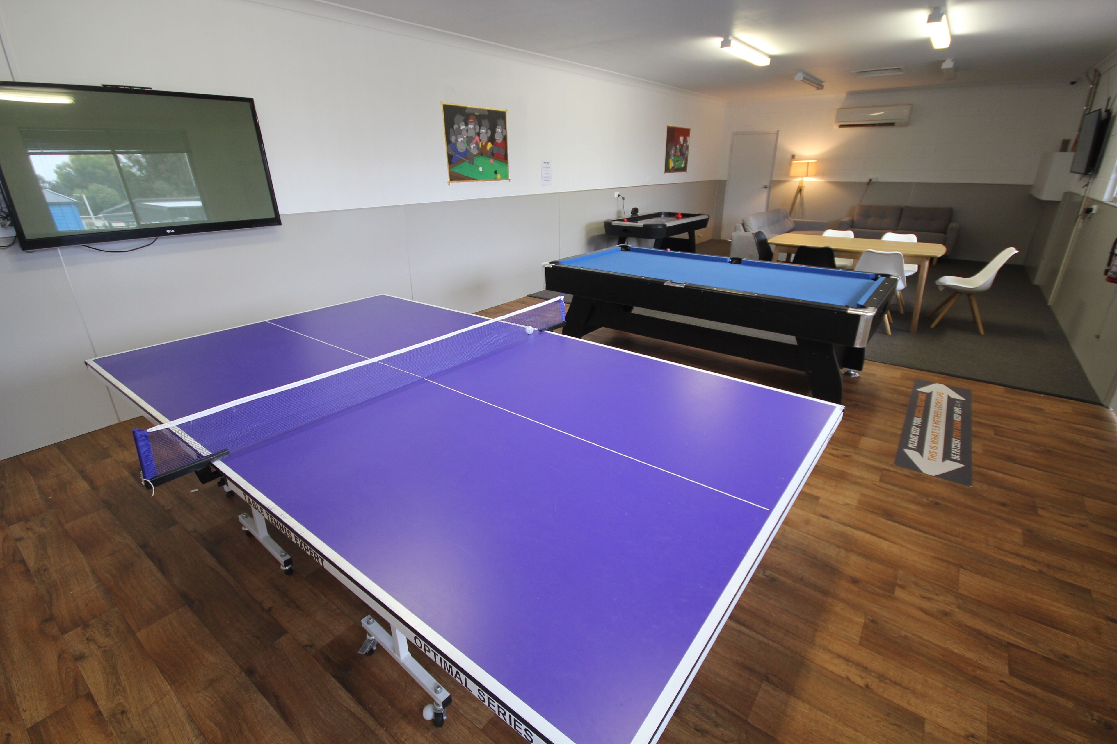 A room with a ping pong table, pool table, and a TV mounted on the wall.
