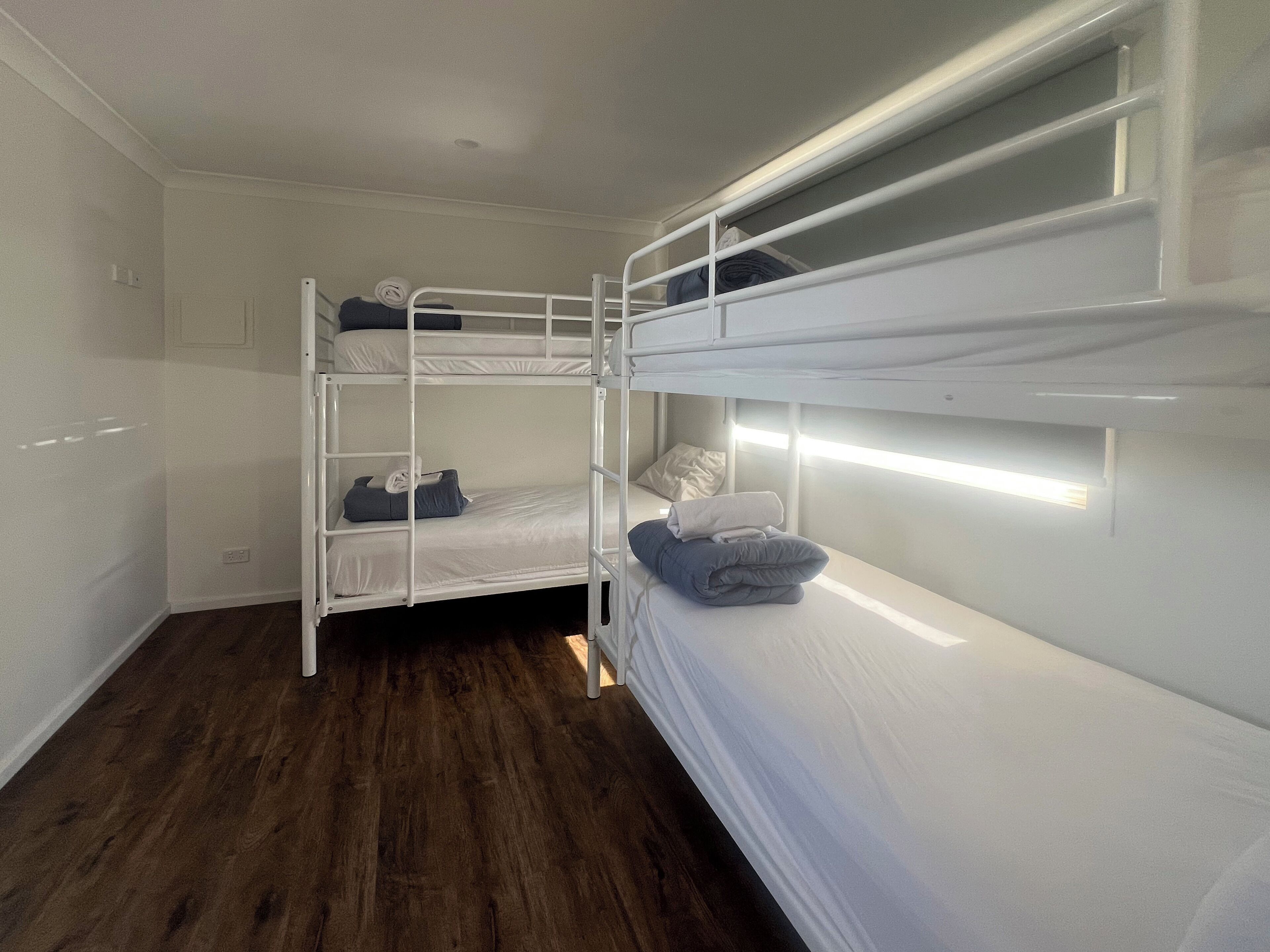 A bunk bed room with a wooden floor, white walls, and a window with blinds.