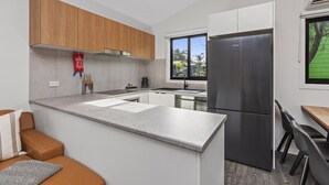 Une cuisine moderne avec des meubles en bois, un réfrigérateur en acier inoxydable, un plan de travail gris et un coin repas comprenant une table et des chaises.