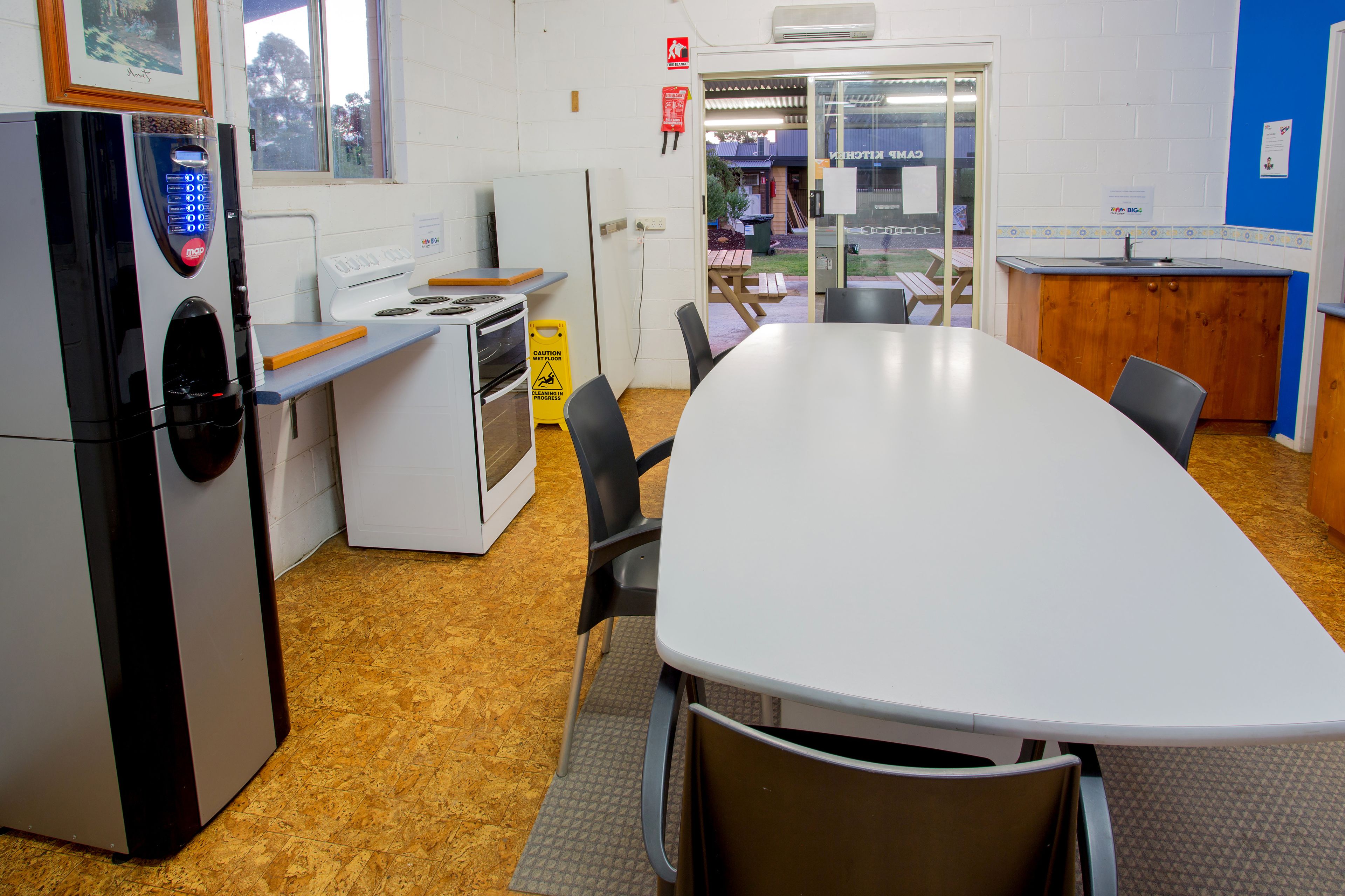 Una cocina con una mesa grande, sillas, un refrigerador y una estufa.