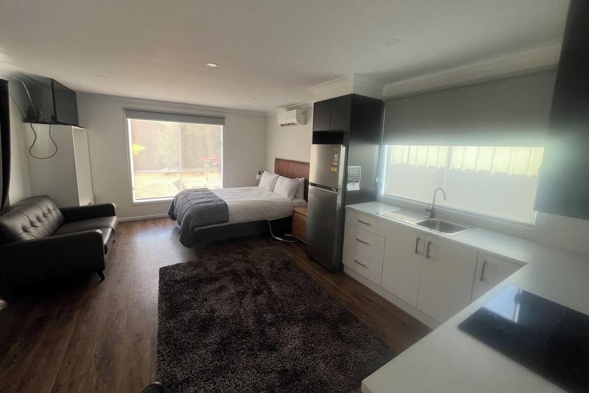 Una habitación pequeña con cama, un sofá cama, una kitchenette y una ventana.