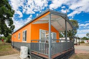 Ein Bungalow mit Veranda, einer kleinen angebauten Garage und blauem Himmel.