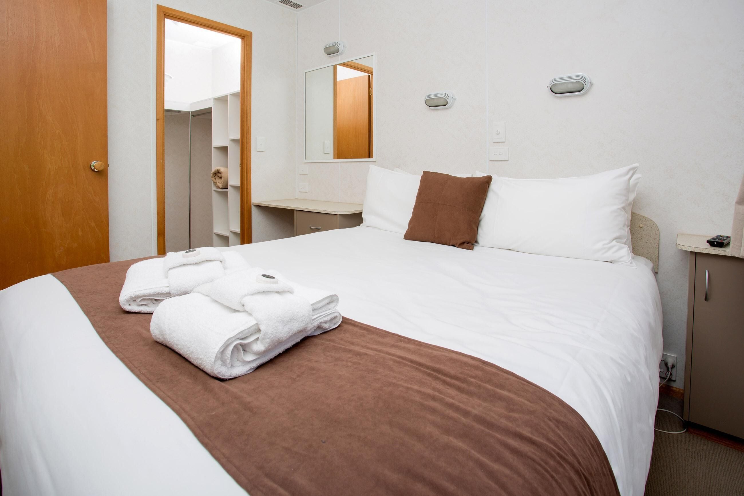 Une chambre d’hôtel avec un lit bien fait, une salle de bain avec un miroir et une table de chevet avec une lampe.
