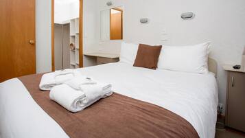 Une chambre d’hôtel avec un lit bien fait, une salle de bain avec un miroir et une table de chevet avec une lampe.