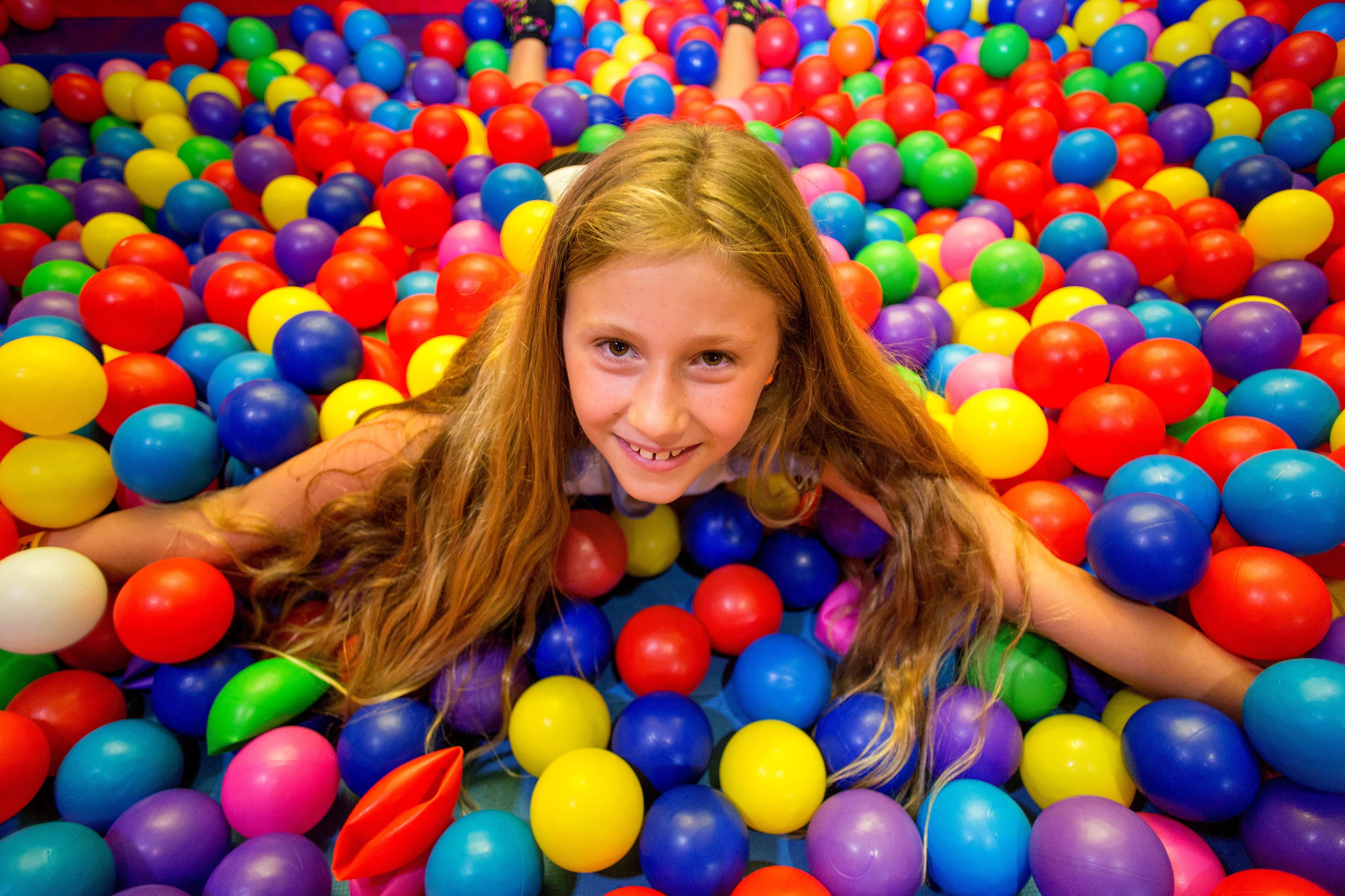 A person lying in a ball pit filled with colorful plastic balls.