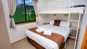 Een slaapkamer met stapelbed, raam, gordijnen en uitzicht op een groen veld.