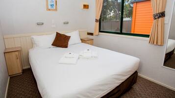 A neatly made bed with white linens and a brown pillow, a wooden nightstand, and a window with curtains.