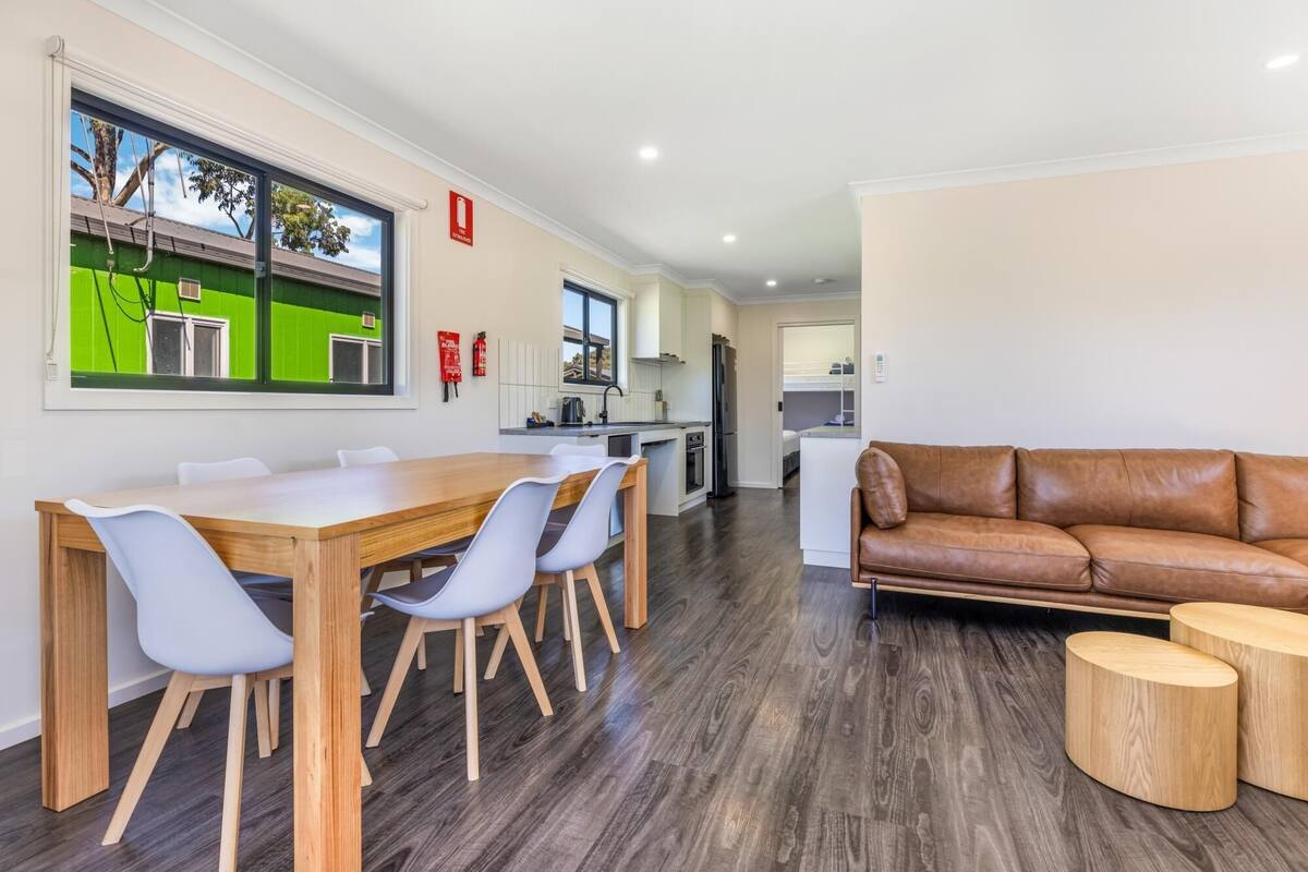 Una cocina moderna con comedor, un sofá de cuero marrón y un amplio ventanal con vistas a un edificio verde.