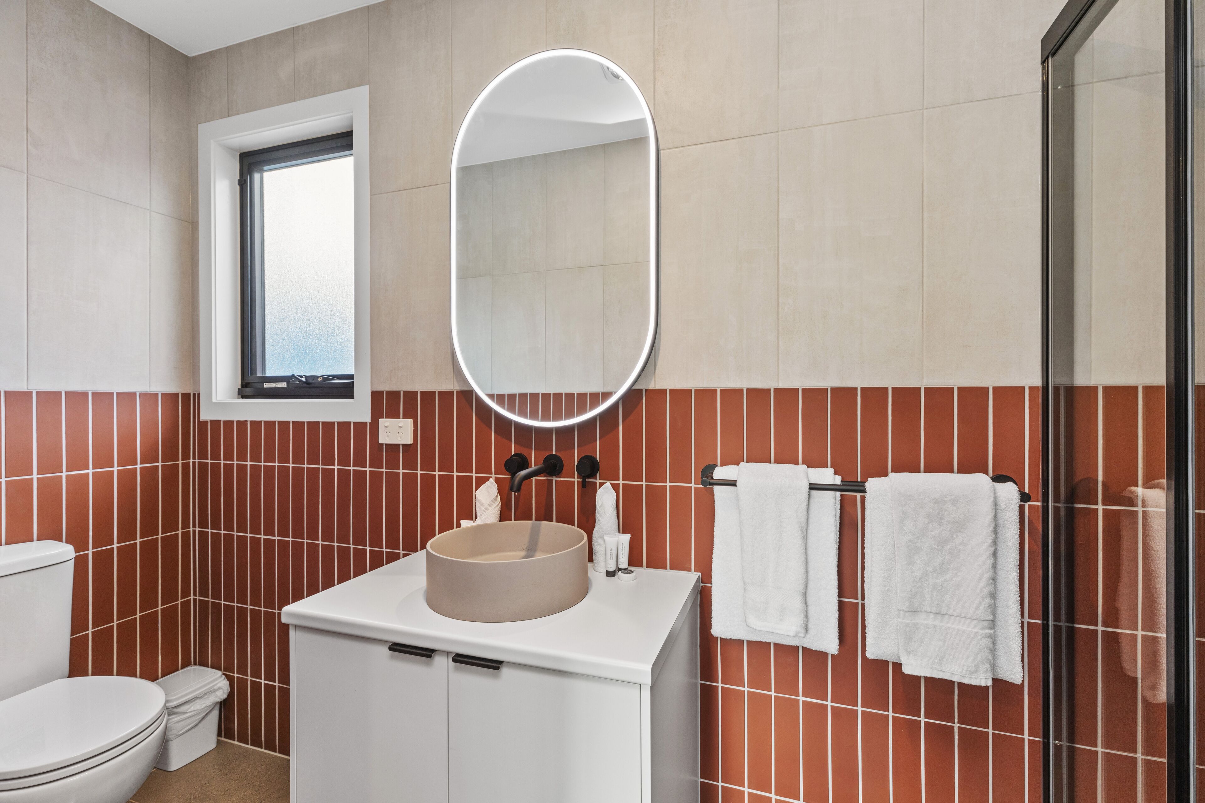 A bathroom with a round sink, white cabinets, a mirror, and a window.