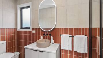 A bathroom with a round sink, white cabinets, a mirror, and a window.