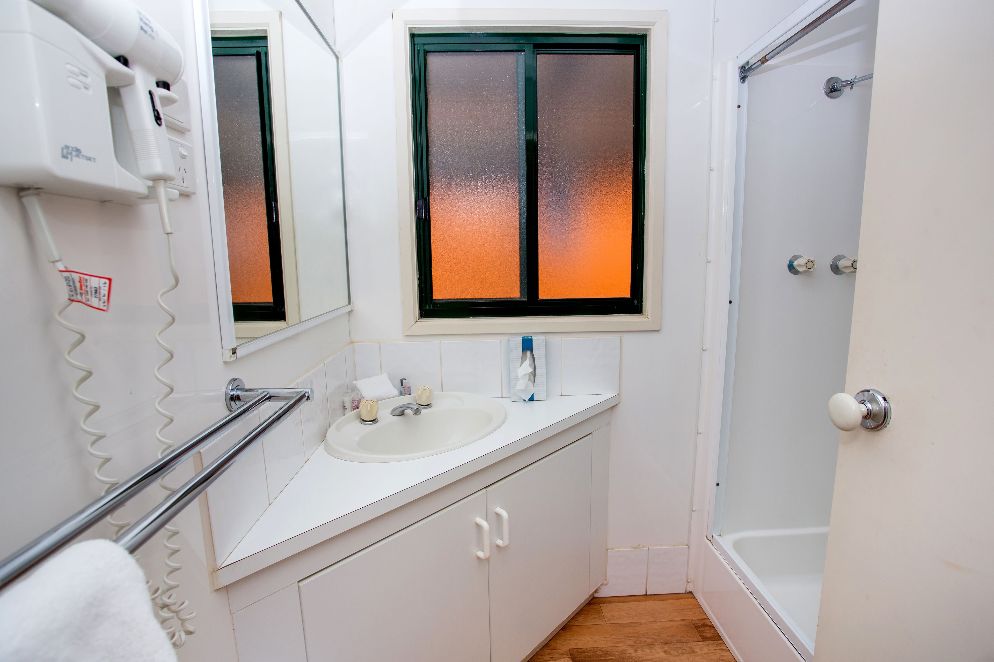 Un baño con lavamanos blanco, un espejo, una ventana con vidrio esmerilado y una ducha.