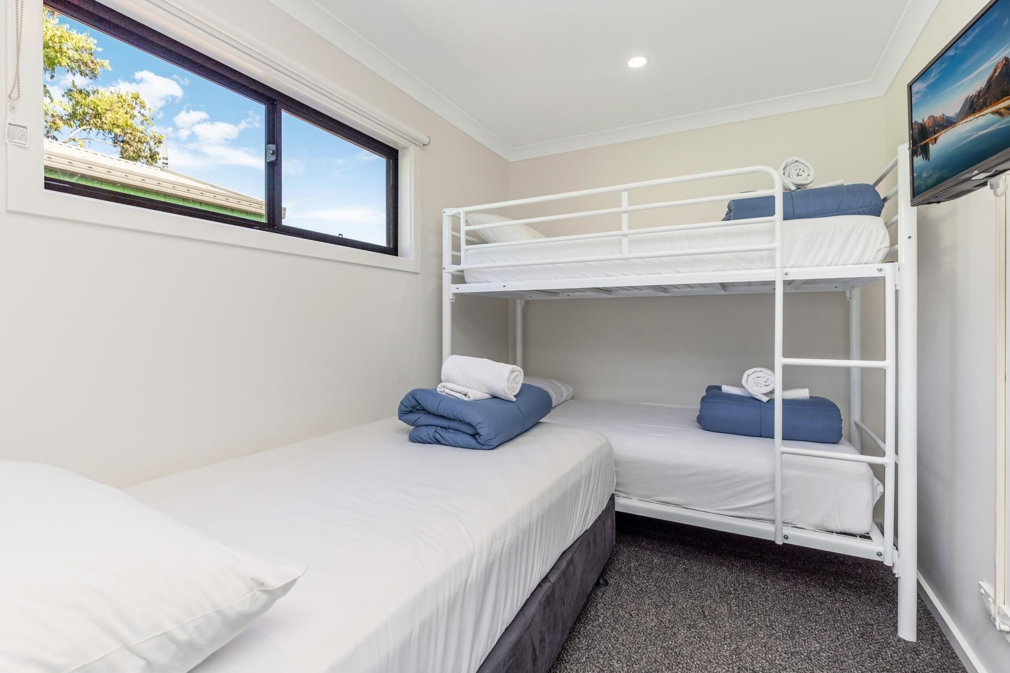 A bunk bed room with white bedding, a window with a view of trees, and a painting on the wall.
