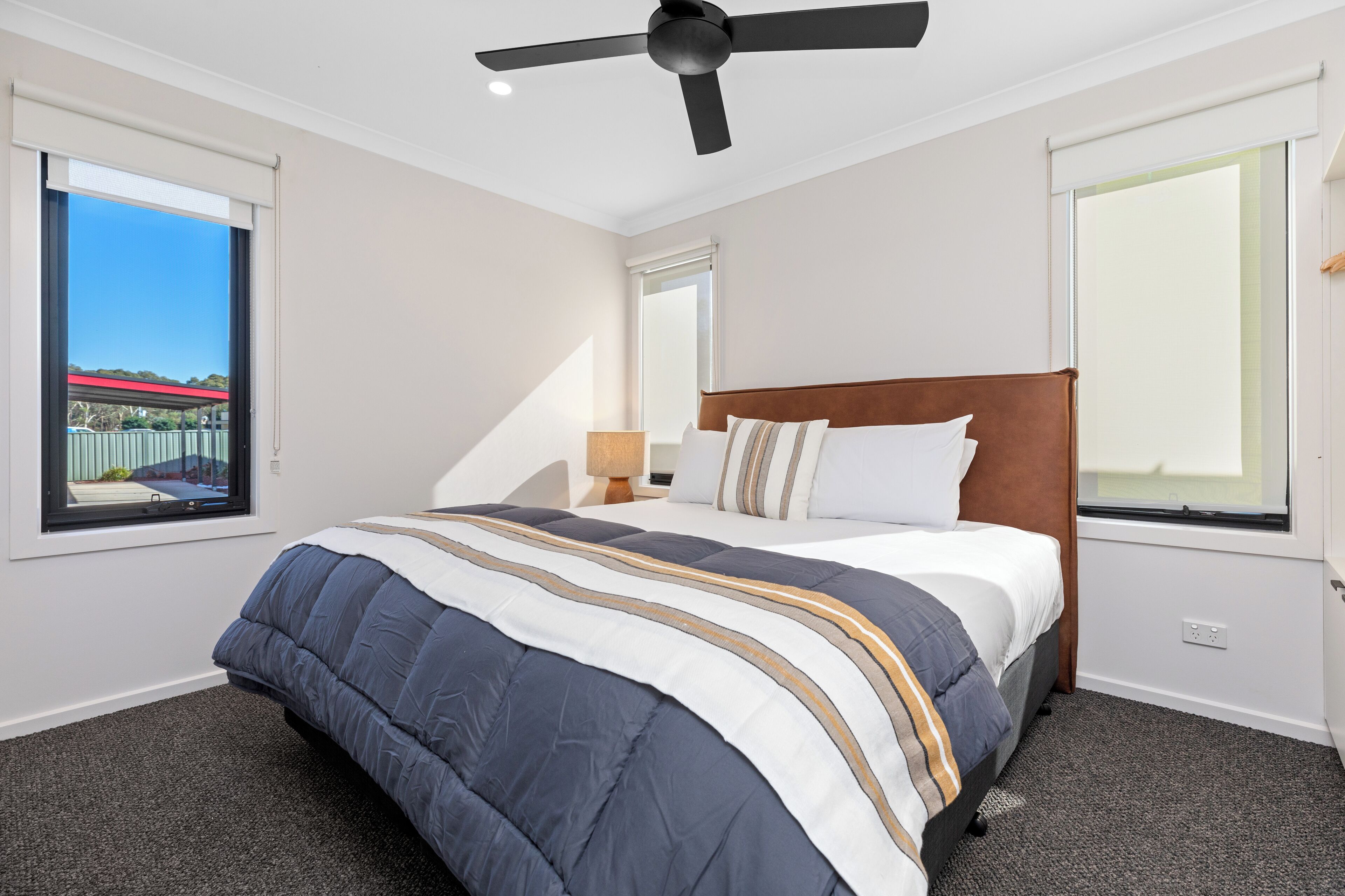 A hotel room with a large bed, a ceiling fan, and a view of a bridge and greenery outside the window.