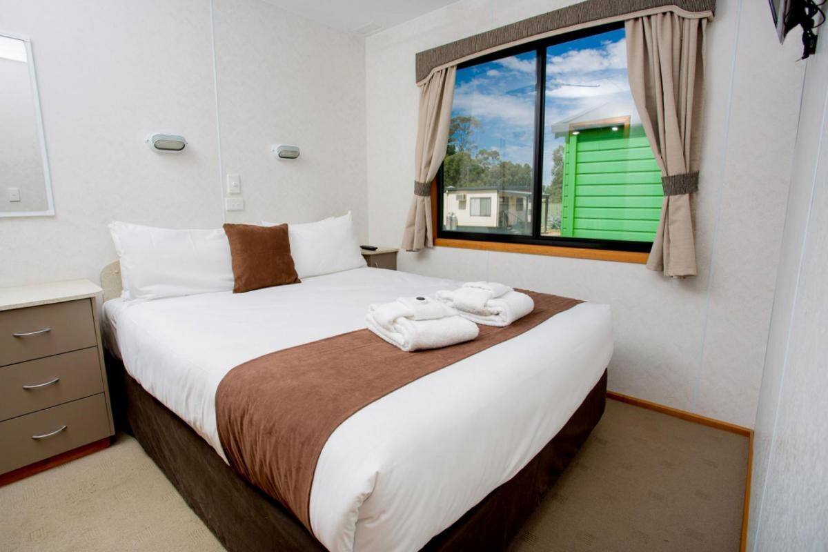 Una habitación de hotel con cama, mesita de noche, cómoda y ventana con cortinas.