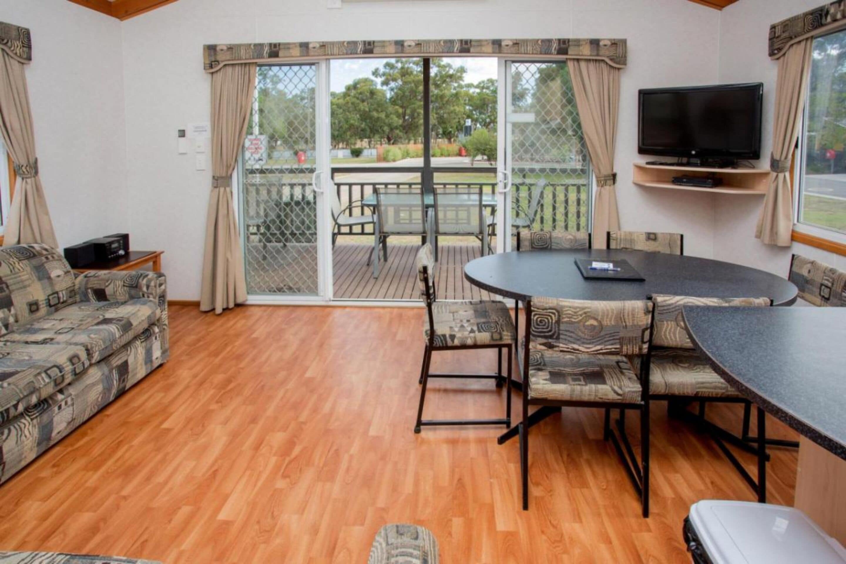 A living room with a sofa, a round table with chairs, a TV, and a sliding glass door leading to an outdoor patio.