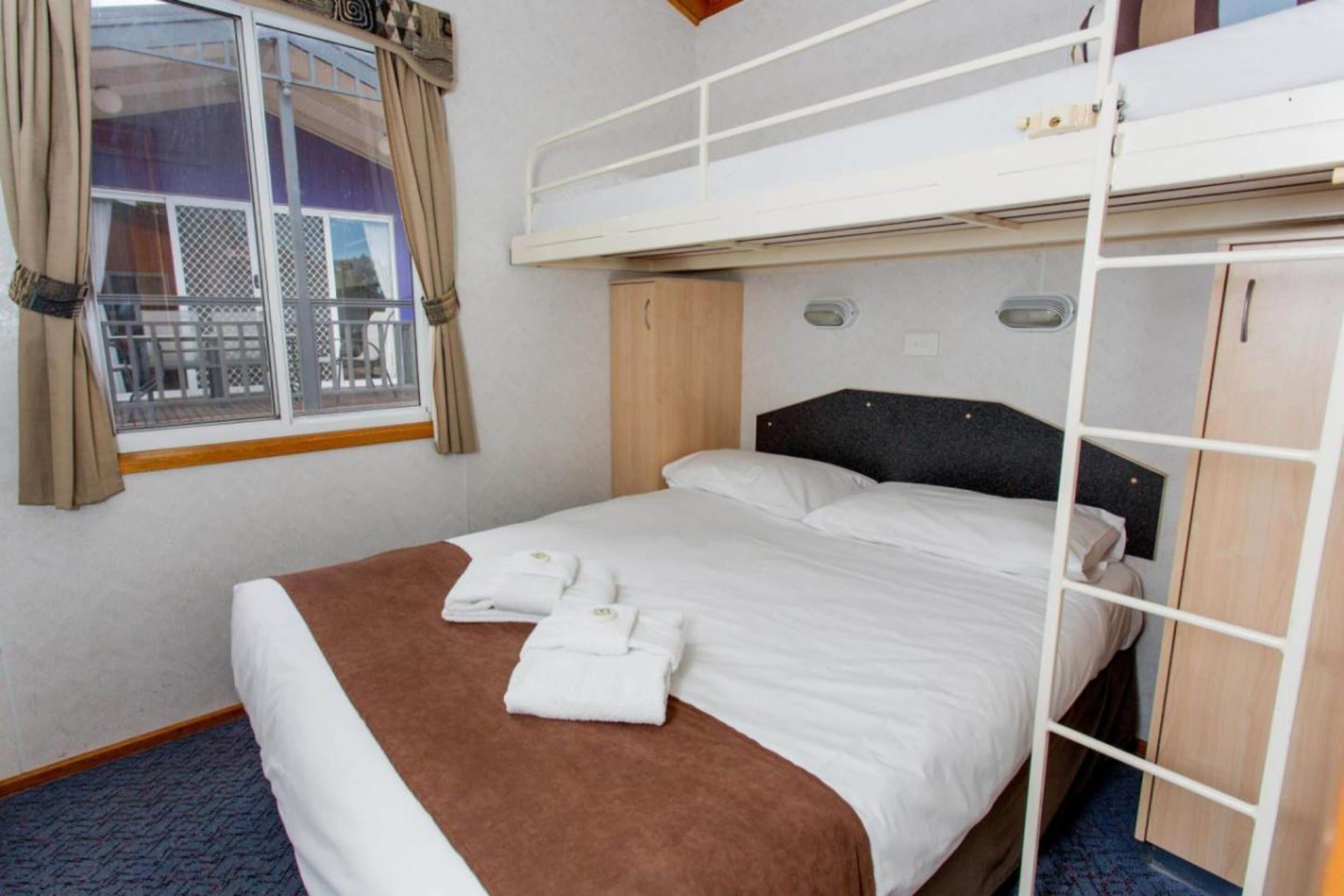 Ein Hotelzimmer mit Etagenbett, einem fensterartigen Blick und einem Bett mit weißer und brauner Bettwäsche, sowie einem blauen Teppich.
