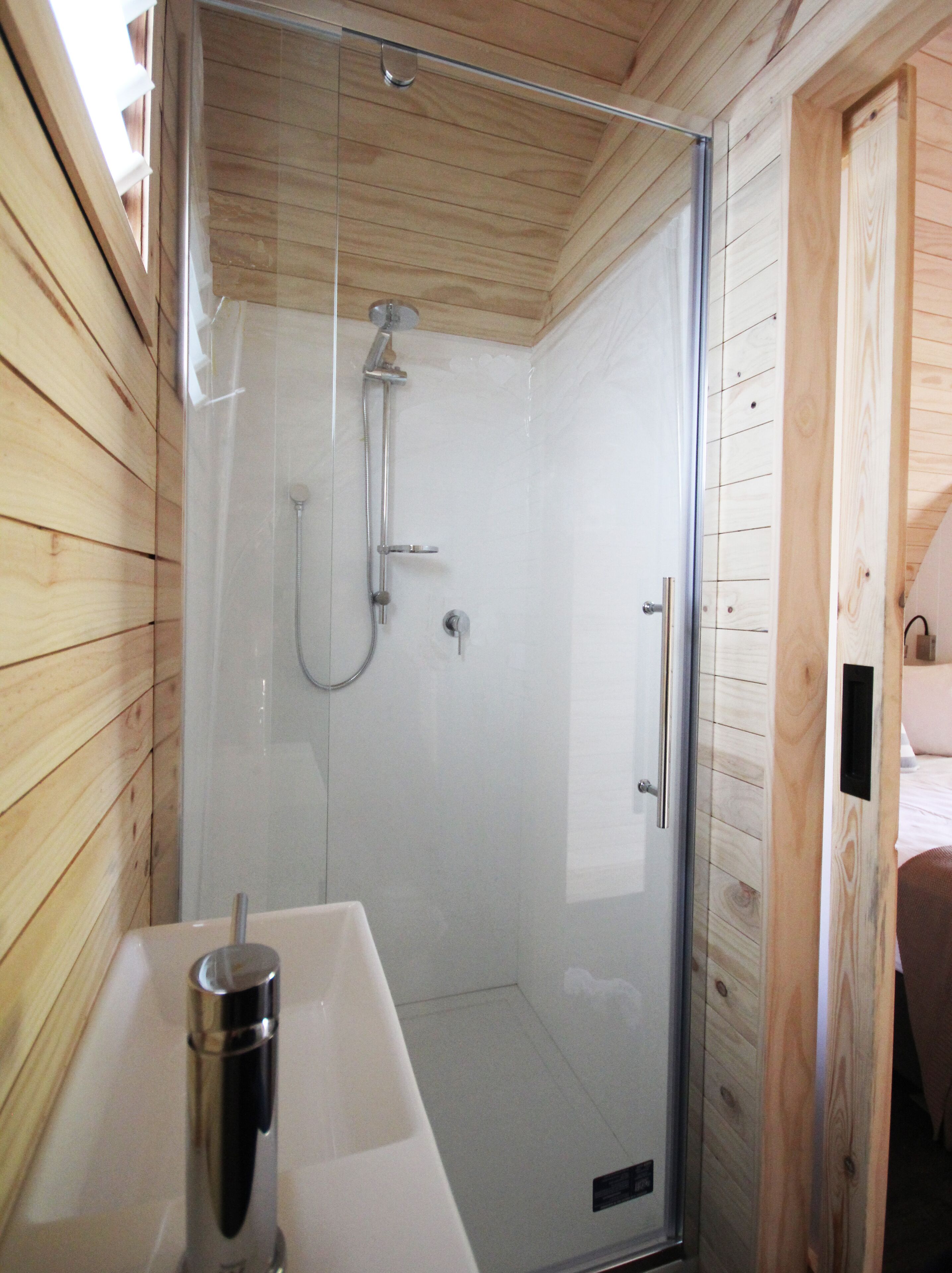 A glass-enclosed shower with a handheld showerhead and a handheld faucet.