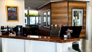 A bar area with a wooden counter, a chalkboard menu, and a beer tap. - Banana Hotel Motel (Banana)