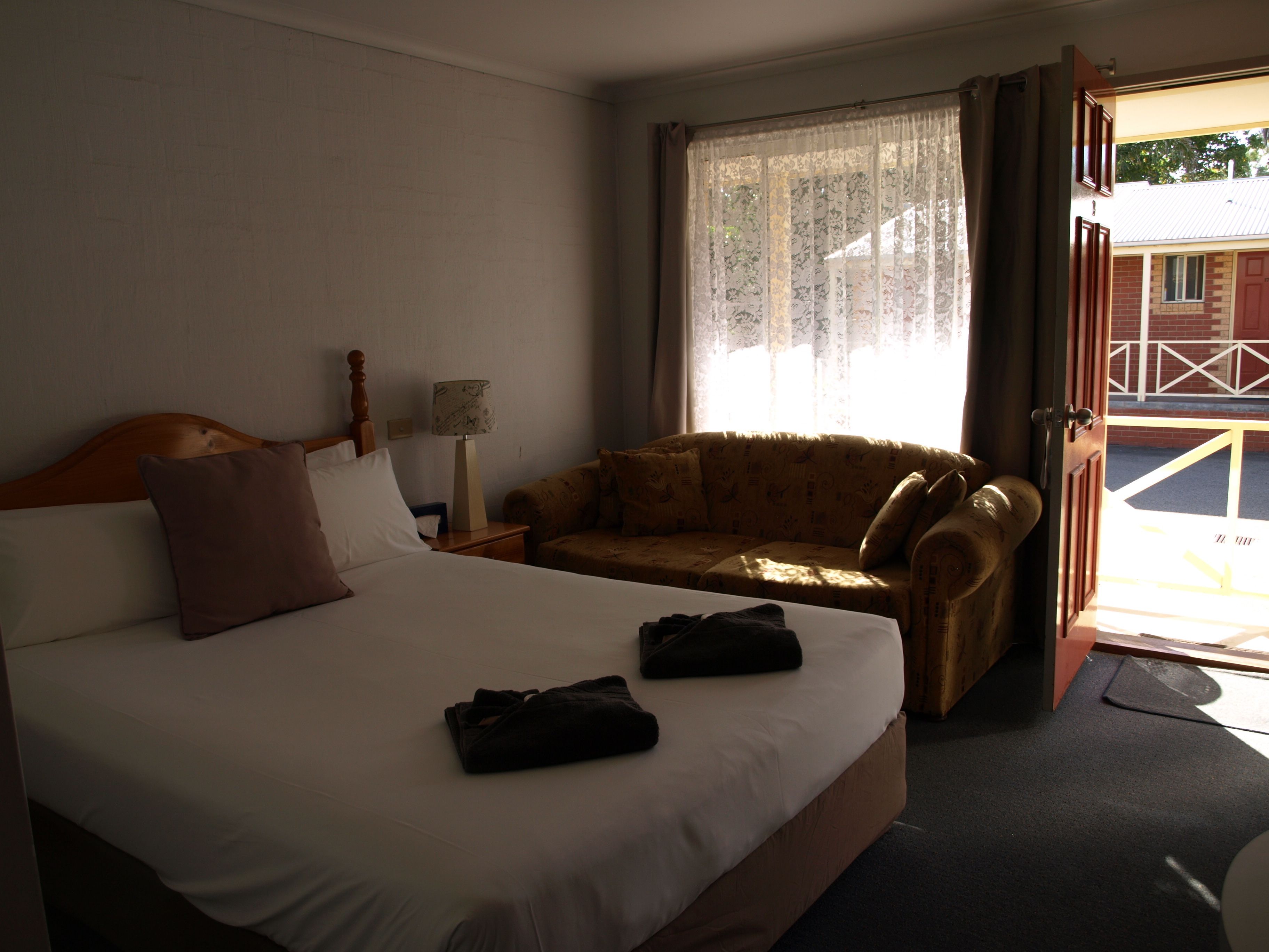 Una habitación de hotel con cama, sofá, mesita de noche, lámpara y ventana con cortinas.