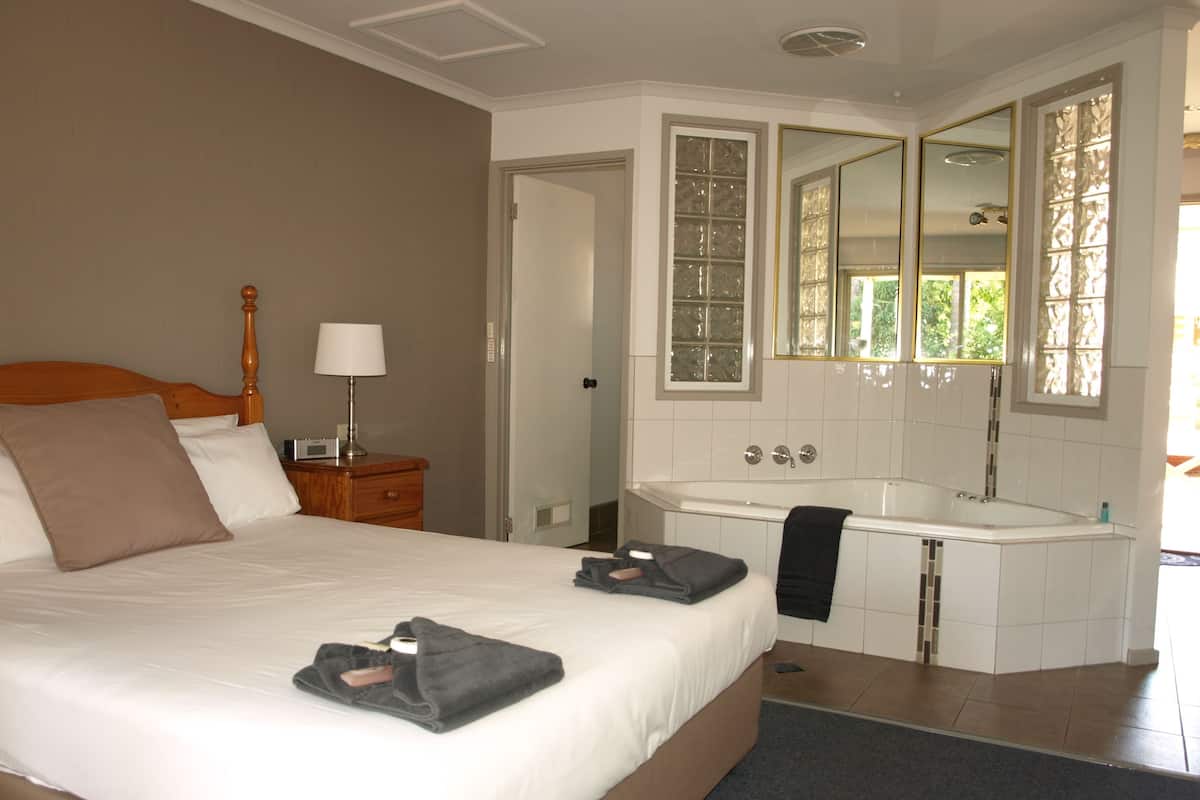 A hotel room with a large bed, a bedside table with a lamp, a bathroom with a bathtub, and a mirror.