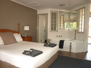 A hotel room with a large bed, a bedside table with a lamp, a bathroom with a bathtub, and a mirror.