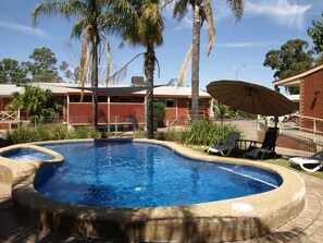 A swimming pool with a stone edge, surrounded by lounge chairs and an umbrella, with a building in the background. - Old Coach Motor Inn Echuca (Echuca)