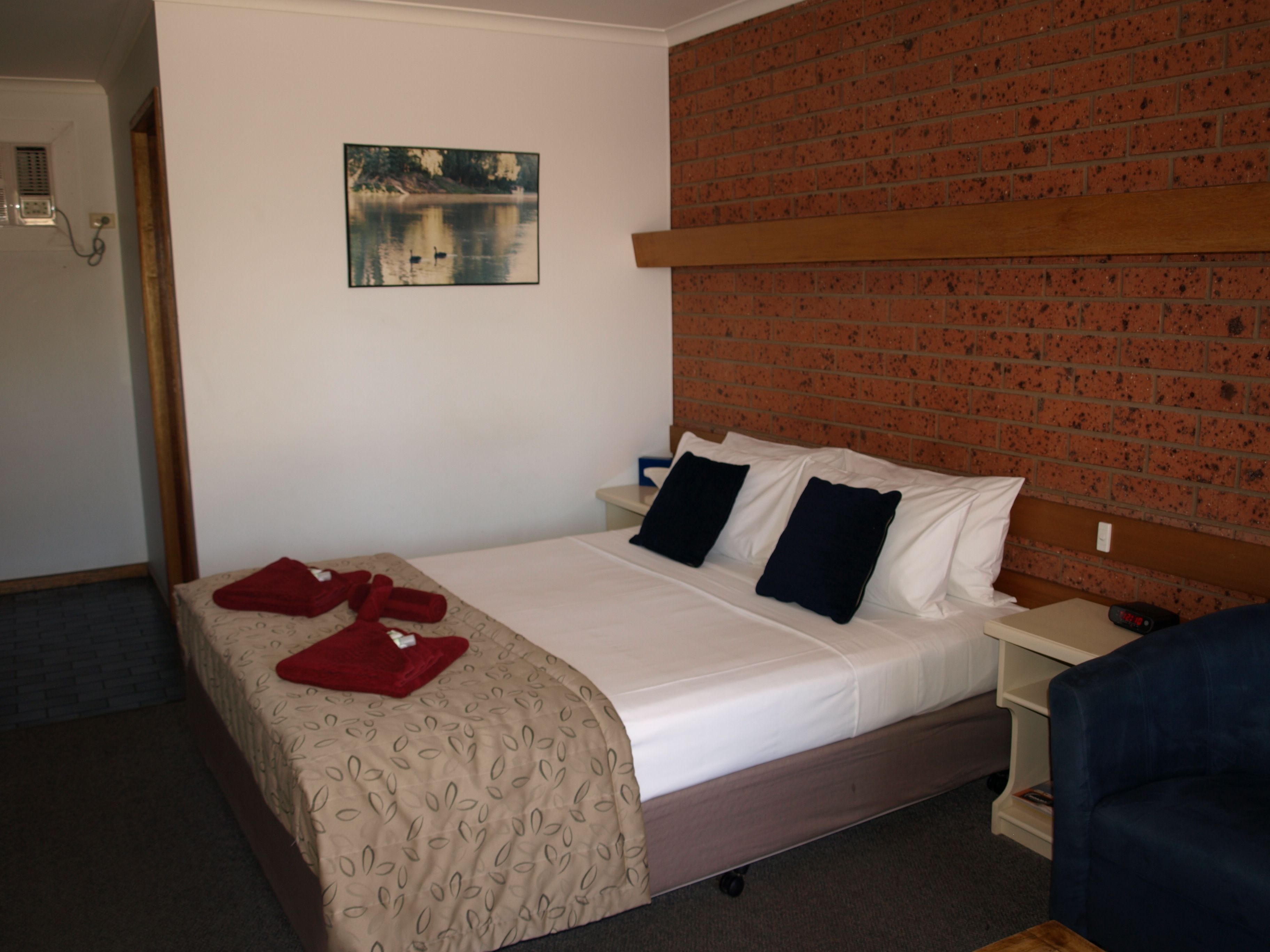 Ein Hotelzimmer mit einem Bett, einem Nachttisch, einer Ziegelwand, einem Gemälde und einem blauen Stuhl.
