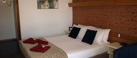 A hotel room with a bed, a nightstand, a brick wall, a painting, and a blue chair.