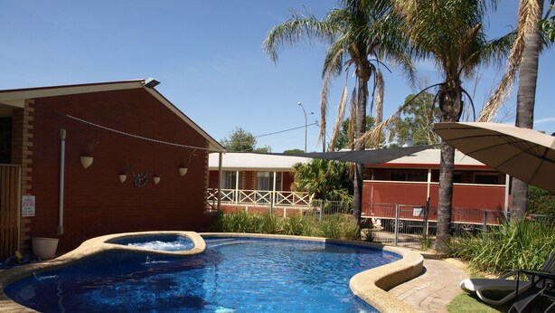 Una piscina con borde de ladrillo, rodeada de palmeras y un edificio de ladrillo.