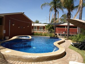 Una piscina con borde de ladrillo, rodeada de palmeras y un edificio de ladrillo.