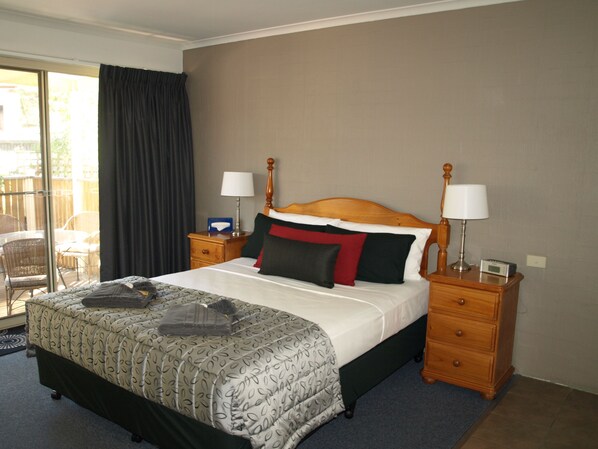 A hotel room with a large bed, two bedside tables, a wooden headboard, and a view of the outdoor patio.