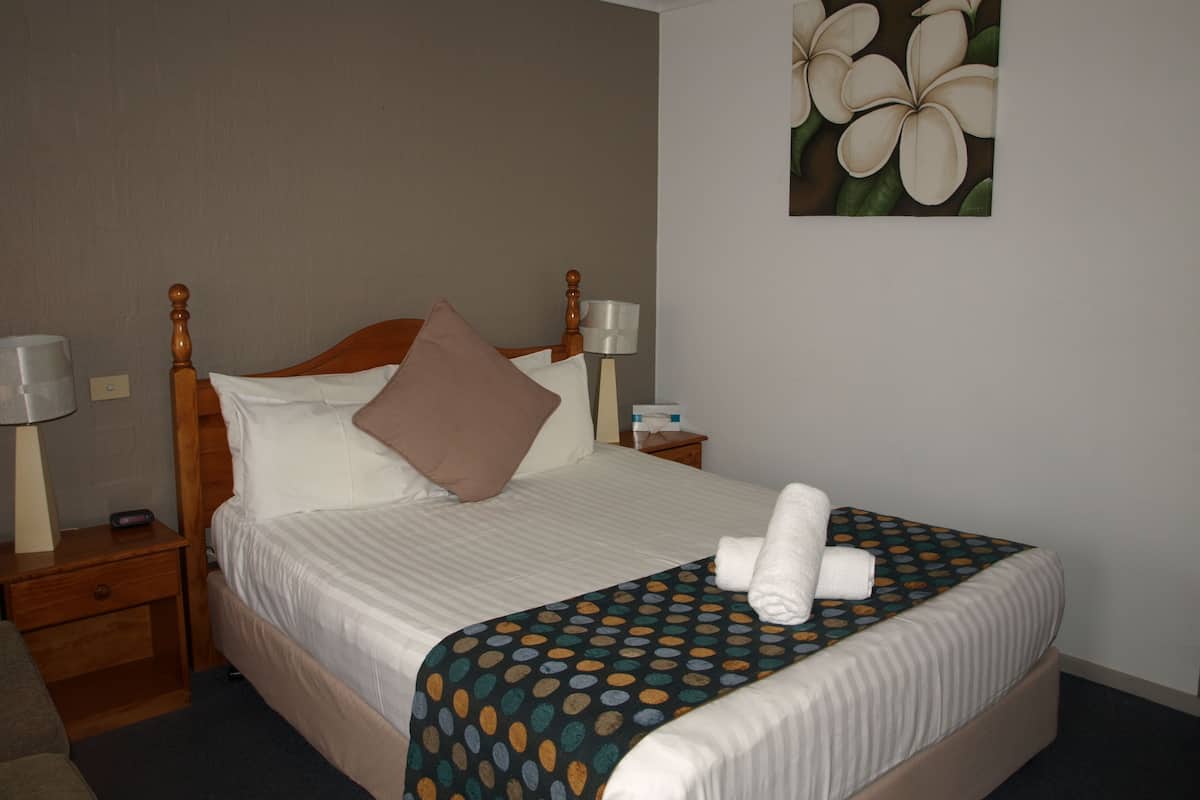 A neatly made bed with a polka dot bedspread, a wooden headboard, and a painting of flowers on the wall.
