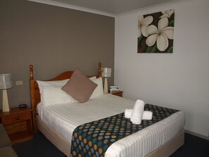 A neatly made bed with a polka dot bedspread, a wooden headboard, and a painting of flowers on the wall. - Old Coach Motor Inn Echuca (Echuca)