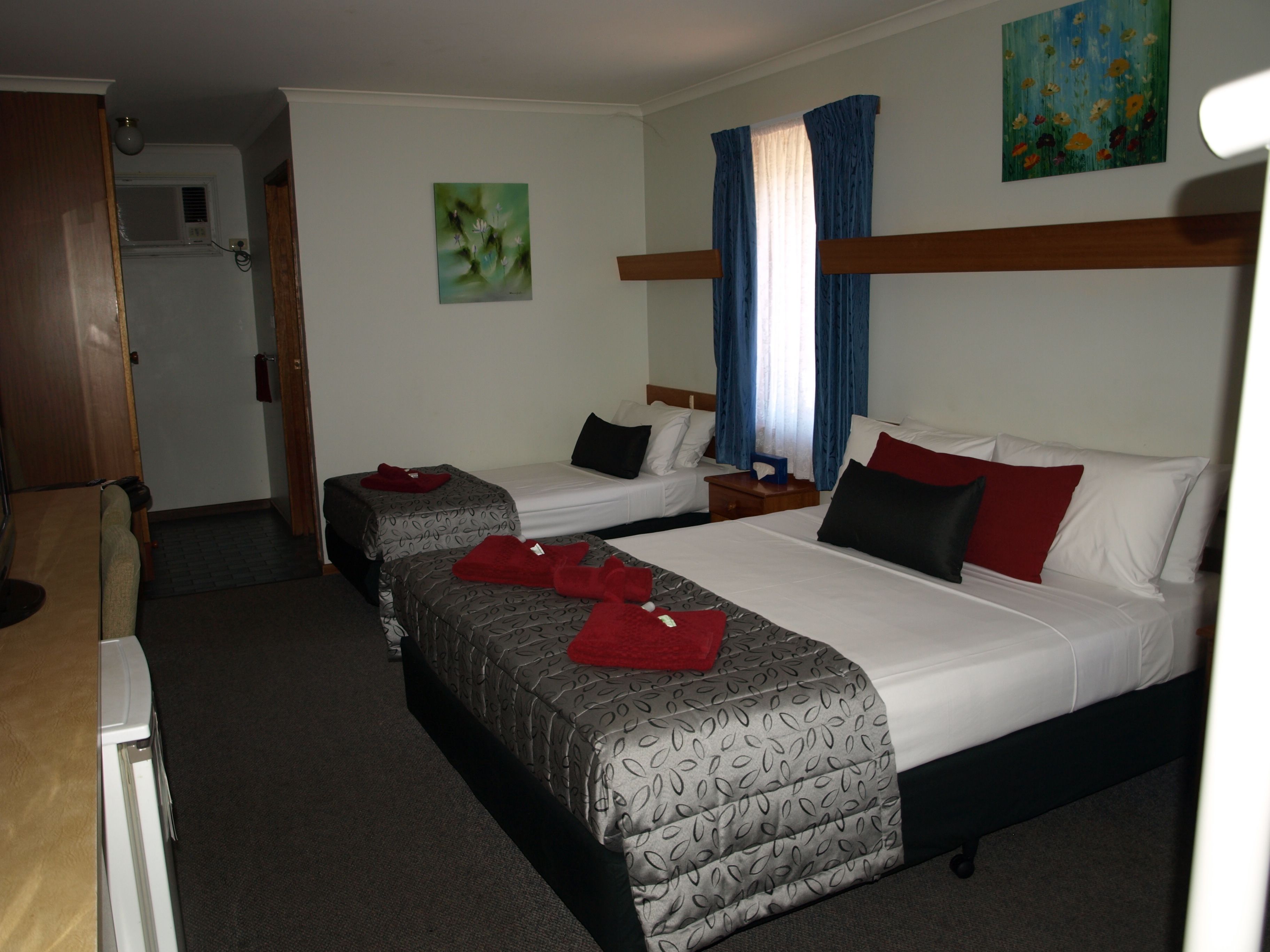 A hotel room with two beds, a small desk, a window with curtains, and a painting on the wall.
